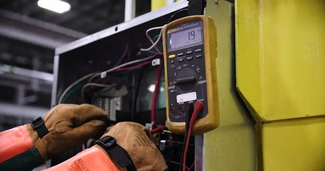 მთავარი Electrician using a multimeter to fix industrial control panel wiring.