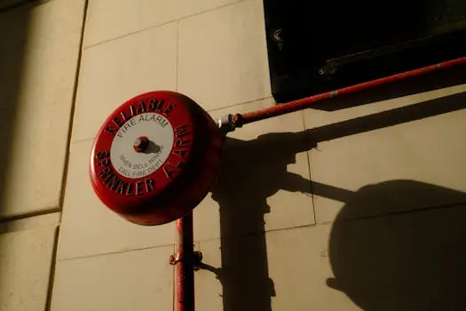 მთავარი A red fire alarm bell with sprinkler system shadow on exterior wall in Hong Kong.